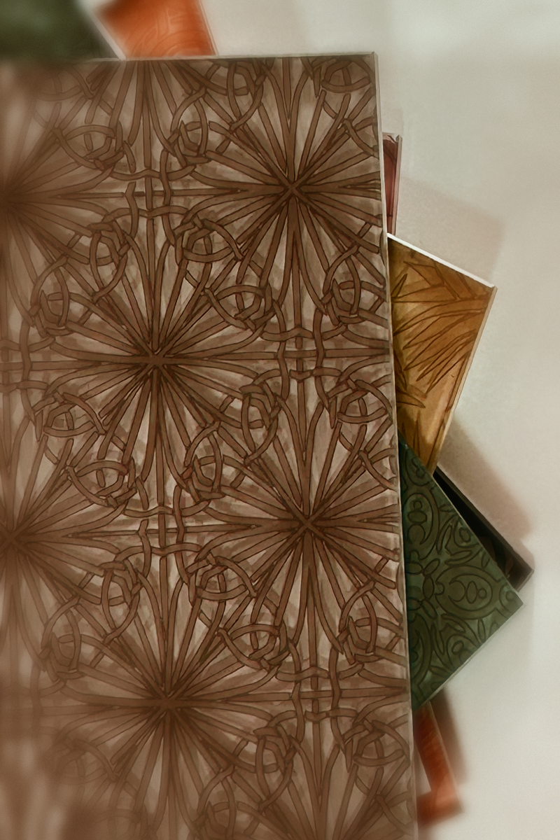 Stack of decorative glass panels showing intricate geometric medallion patterns in warm brown, amber, and green tones